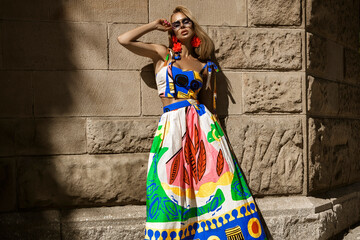 Beautiful female model in a colorful summer dress and sexy high heels poses sensually in the city...