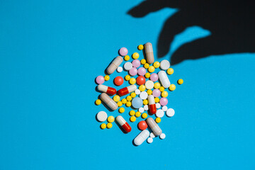 Shadow from hand taking a pill from the heap of pills on blue background.