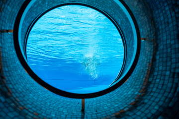 Woman Swimming in the Ship Porthole in Underwater in Swimming Pool in a Sunny Day in Switzerland.