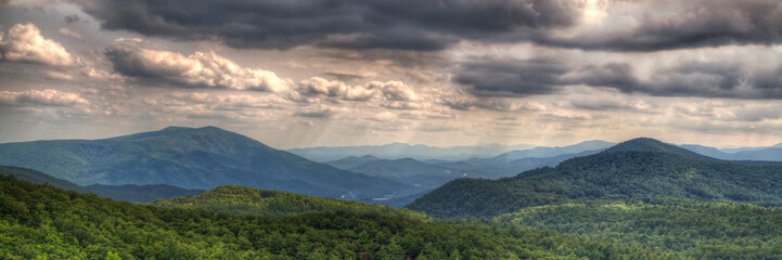 Smoky Mountains National Park.  Layers of hilly terrain stretch into the distance beneath a dramatic, cloud-filled sky. The lush greenery on the hills indicates a vibrant forest area.
