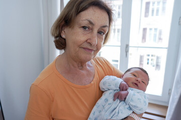 Proud grandmother holding her newborn grandchild wrapped in a cozy blanket, both looking content...