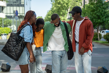 Cheerful contented african american four friends girls and guys laughing urban walking together....