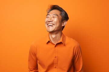 Fototapeta premium Portrait of a glad asian man in his 40s laughing isolated on soft orange background