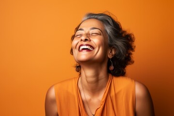 Portrait of a satisfied indian woman in her 50s laughing isolated in soft orange background