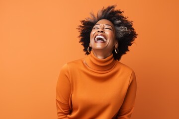 Obraz premium Portrait of a content afro-american woman in her 50s laughing isolated on soft orange background