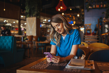 A female nurse in blue scrubs enjoys a relaxing moment, browsing her phone at a cozy cafe table...