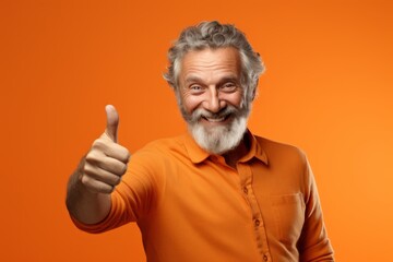 Naklejka premium Portrait of a smiling man in his 50s showing a thumb up over soft orange background