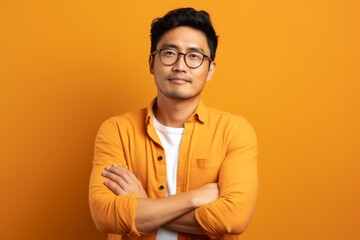 Portrait of a content asian man in his 20s with arms crossed in soft orange background