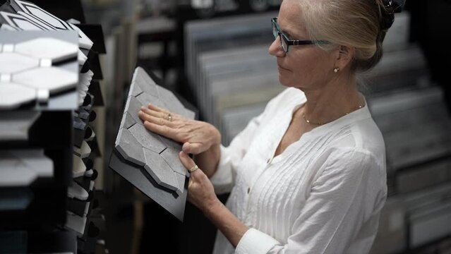 Attractive mature woman shopping for wall tile looking through samples for home redecorating renovation project, in a hardware store.