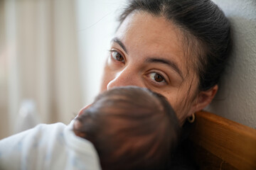 Close-up of a mother holding her newborn baby with her eyes open, capturing the deep bond and...