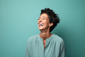 Obraz premium Portrait of a grinning indian woman in her 40s laughing on soft teal background
