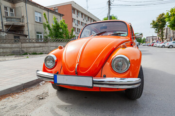 Vintage small orange car standing by the side of the road.