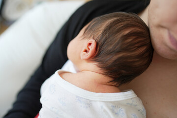 Newborn baby resting on mother's chest, detailed shot showing baby's head, mother in background,...