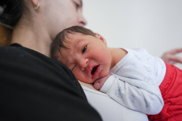 Newborn baby lying on mother's chest, one eye open, slightly awake, tender maternal moment, mother...