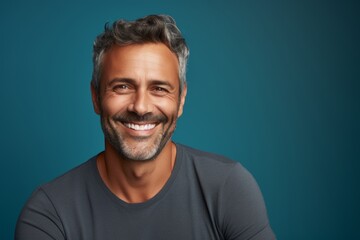 Obraz premium Portrait of a happy man in his 40s smiling at the camera while standing against soft teal background