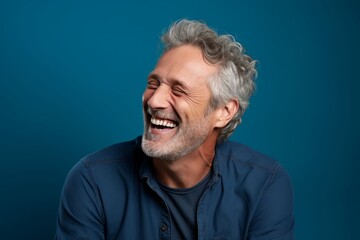 Portrait of a happy man in his 50s laughing isolated on soft teal background
