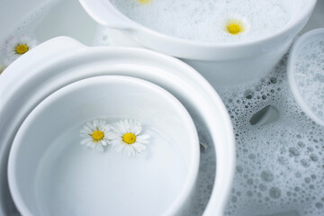 White dishes are filled with water and foam. Close-up of flowers on wet dishes. Place for text. Chamomiles in foam