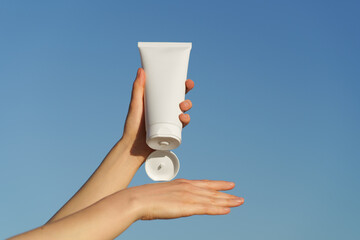 Female hands apply cream from white jar mockup on hand against blue sky background. Concept of skin...
