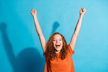 Photo of young successful red haired girl in orange t shirt raised fists up celebrating victory...