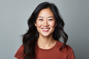 Portrait of a grinning asian woman in her 30s smiling at the camera isolated on soft gray background