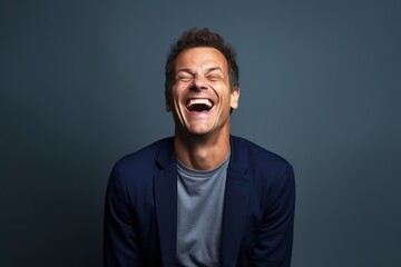 Portrait of a grinning man in his 40s laughing in front of soft gray background