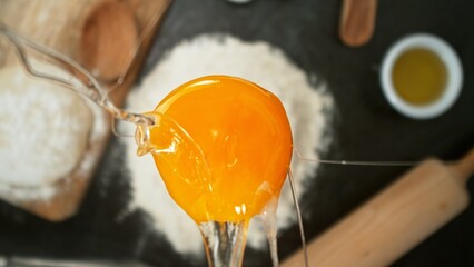 close up view of yolk falling on flour on black stone table