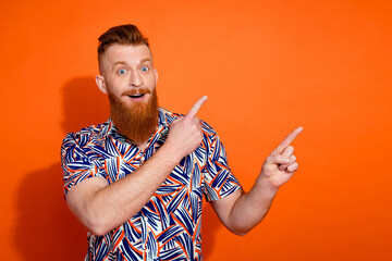 Photo of funky excited guy dressed print shirt pointing two fingers emtpy space isolated orange color background