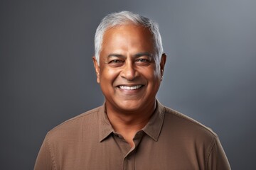Obraz premium Portrait of a satisfied indian man in his 60s smiling at the camera isolated in soft gray background