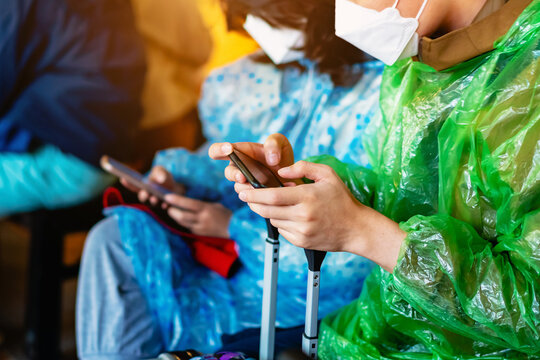 Hands of young man wear face mask and green raincoat with luggage using smartphone search map to find travel directions. Preventive care and health care during travel concept. Technology and journey.