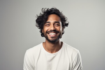 Fototapeta premium Portrait of a joyful indian man in his 20s smiling at the camera in front of soft gray background