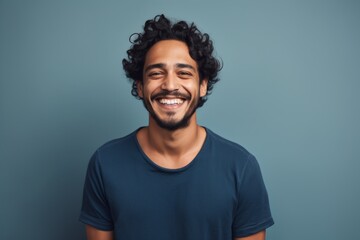 Fototapeta premium Portrait of a joyful indian man in his 20s smiling at the camera over soft gray background