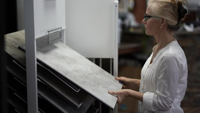 Happy mature woman running hand across touching luxury vinyl tile samples in a floor store for a home remodeling project.