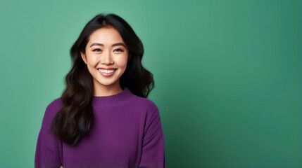Obraz premium A photo of a young Asian woman smiling. She is wearing a purple sweater. The background is green.