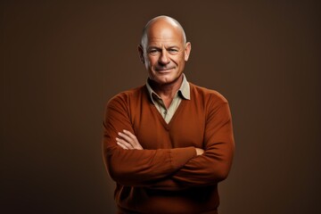 Obraz premium Portrait of a jovial man in his 50s with arms crossed isolated on soft brown background