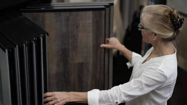 Happy mature woman touching luxury vinyl tile plank samples in a floor store for a home remodeling renovation project.