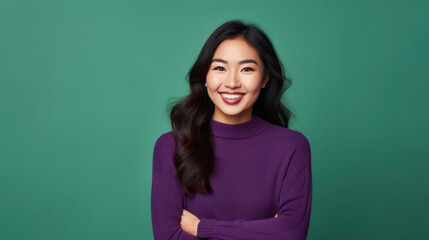 Fototapeta premium A young woman with long black hair and a purple turtleneck smiling at the camera with her arms crossed.