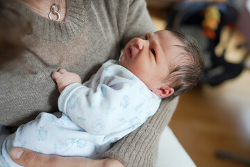 Newborn baby resting in an adult's arms, gazing upwards with curiosity, capturing a serene moment...