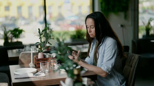 In a cafe, a middle-aged woman is relaxing, chatting on social networks on her phone. She enjoys the comfort and virtual communication.