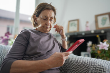 Senior woman with short hair wearing a grey shirt, sitting on a couch and examining her red...