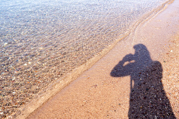 Portrait woman's shadow on sandy beach, with waves gently lapping against the shore and pebbles...