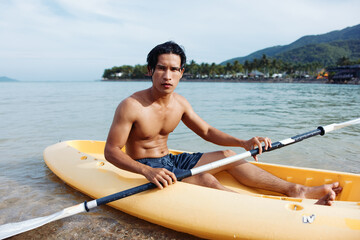Happy Asian Man Enjoying Kayaking Adventure on Tropical Beach