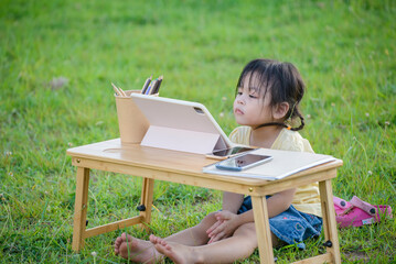 Asian preschool children using digital tablet with stylus pen write and do homework outdoor. Thai...