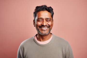 Portrait of a satisfied indian man in his 40s smiling at the camera while standing against pastel...