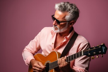Portrait of a content man in his 50s playing the guitar in front of pastel or soft colors background