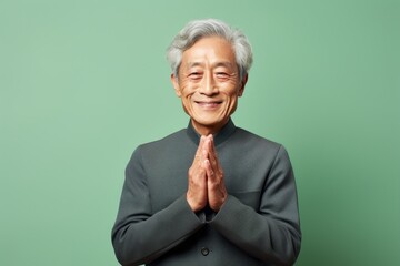 Portrait of a content asian man in his 80s joining palms in a gesture of gratitude isolated on pastel or soft colors background