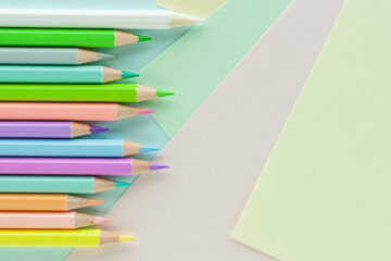 Pastel colored pencils in uneven row on sheets of colored paper