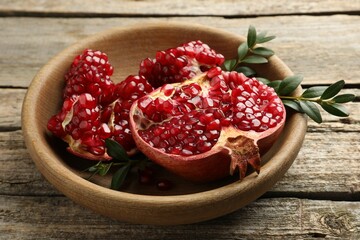 Cut fresh pomegranate and green leaves on wooden table, closeup