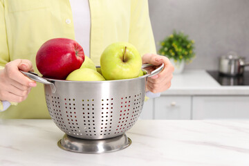 Woman holding colander with fresh apples at white marble table in kitchen, closeup. Space for text