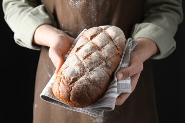 Woman holding freshly baked bread on black background, closeup