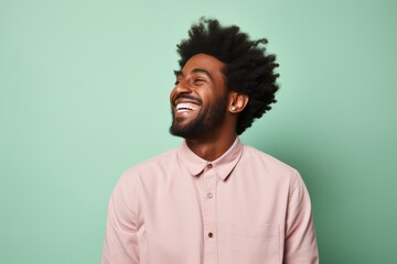 Fototapeta premium Portrait of a content afro-american man in his 20s laughing in front of pastel or soft colors background